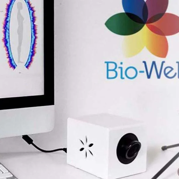 Hvit, kubeformet Bio-Well-enhet foran en dataskjerm med Bio-Well-logoen og fargede ringer