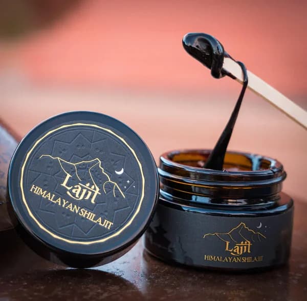 Svart rund boks merket «Himalayan Shilajit» ved siden av en skje med en svart, tykk masse, mot rød bakgrunn
