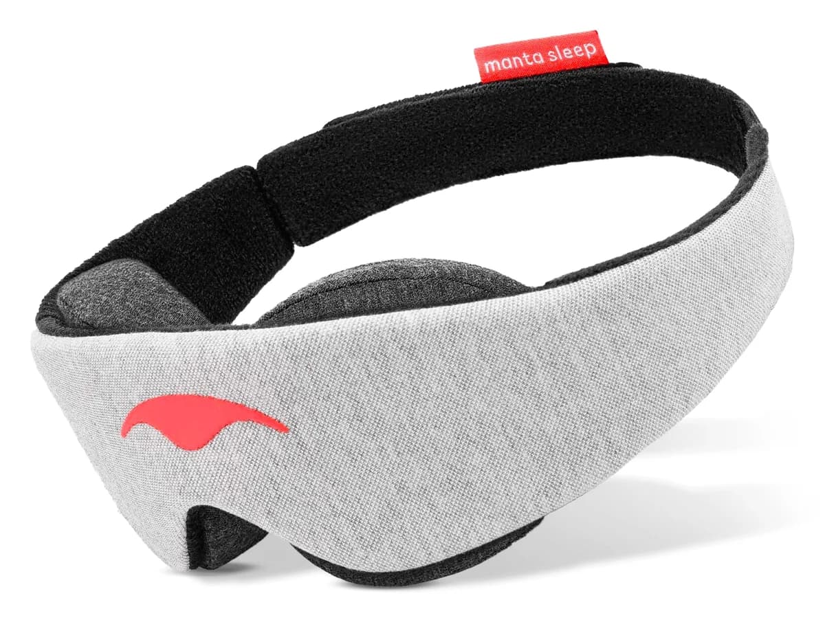 Grå Manta Sleep Mask med svart elastisk bånd og lite rødt merke, sett på skrå forfra