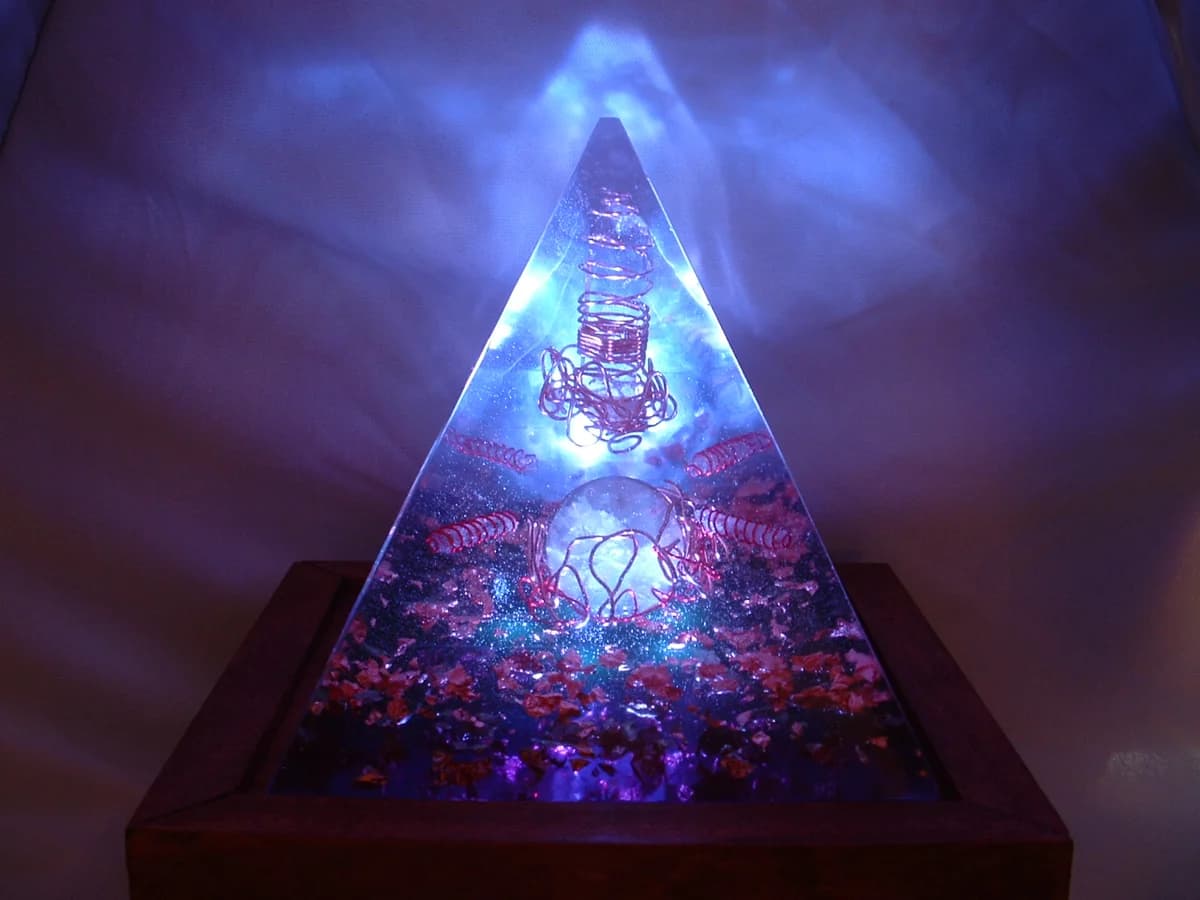 Opplyst orgonitt-pyramide med harpiks, metallspon og krystaller, på et trebrett