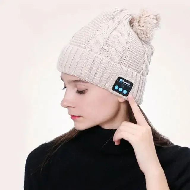 Kvinne med lys strikket lue med bluetooth-lyd og pompong, sett fra siden