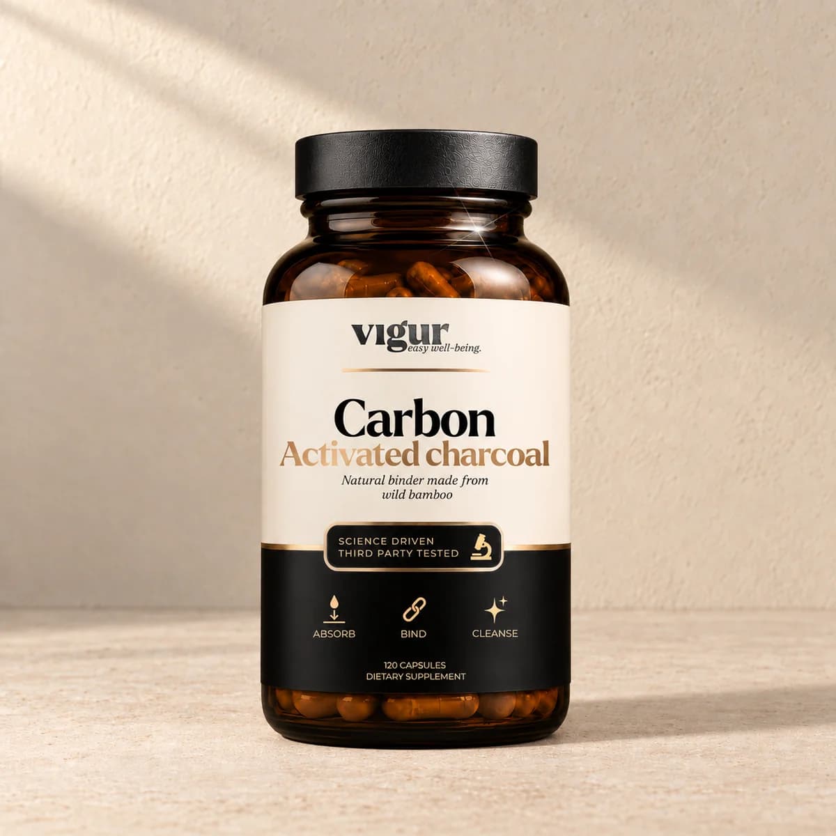 Mørk brun glassboks med svart lokk og lys etikett merket Vigur og «Carbon Activated charcoal» på beige bakgrunn