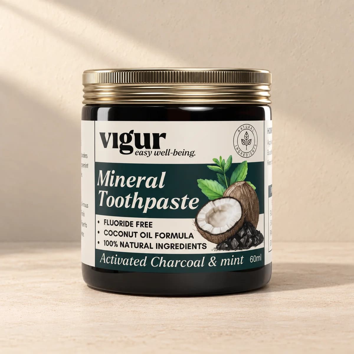 Svart glasskrukke med gullkant og lys etikett «Mineral Toothpaste Activated charcoal & mint» fra Vigur på beige bakgrunn