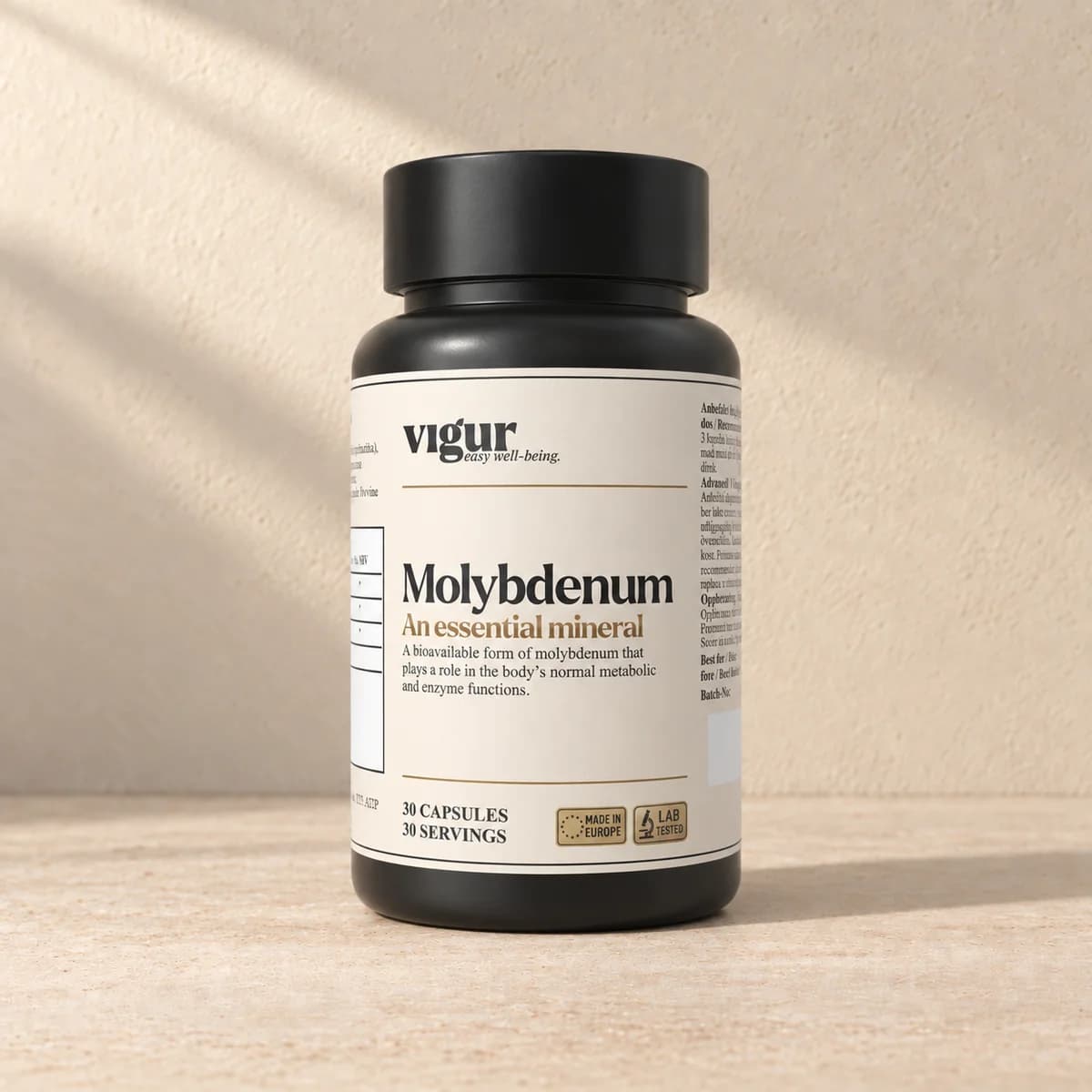 Svart tilskuddsboks med lys etikett merket Vigur og «Molybdenum» på beige bakgrunn