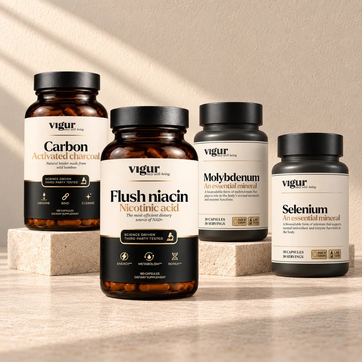 Fire Vigur-produkter: to svarte kapselbokser, en mørk brun boks «Flush niacin» og en mørk boks «Carbon», på en lys sokkel mot beige bakgrunn