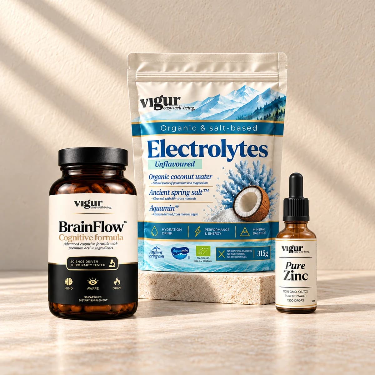 Tre Vigur-produkter side om side: en mørk kapselboks «BrainFlow», en lys pose med elektrolytter og en liten dråpeflaske med sink, på beige bakgrunn
