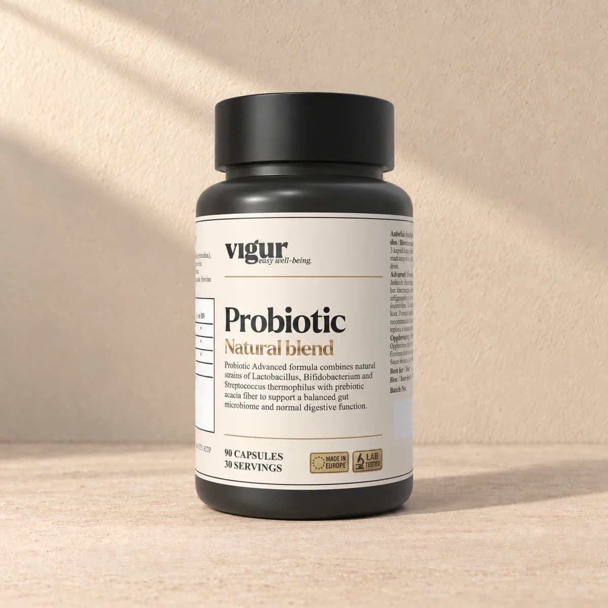 Svart tilskuddsboks med lys etikett merket Vigur og «Probiotic» på beige bakgrunn