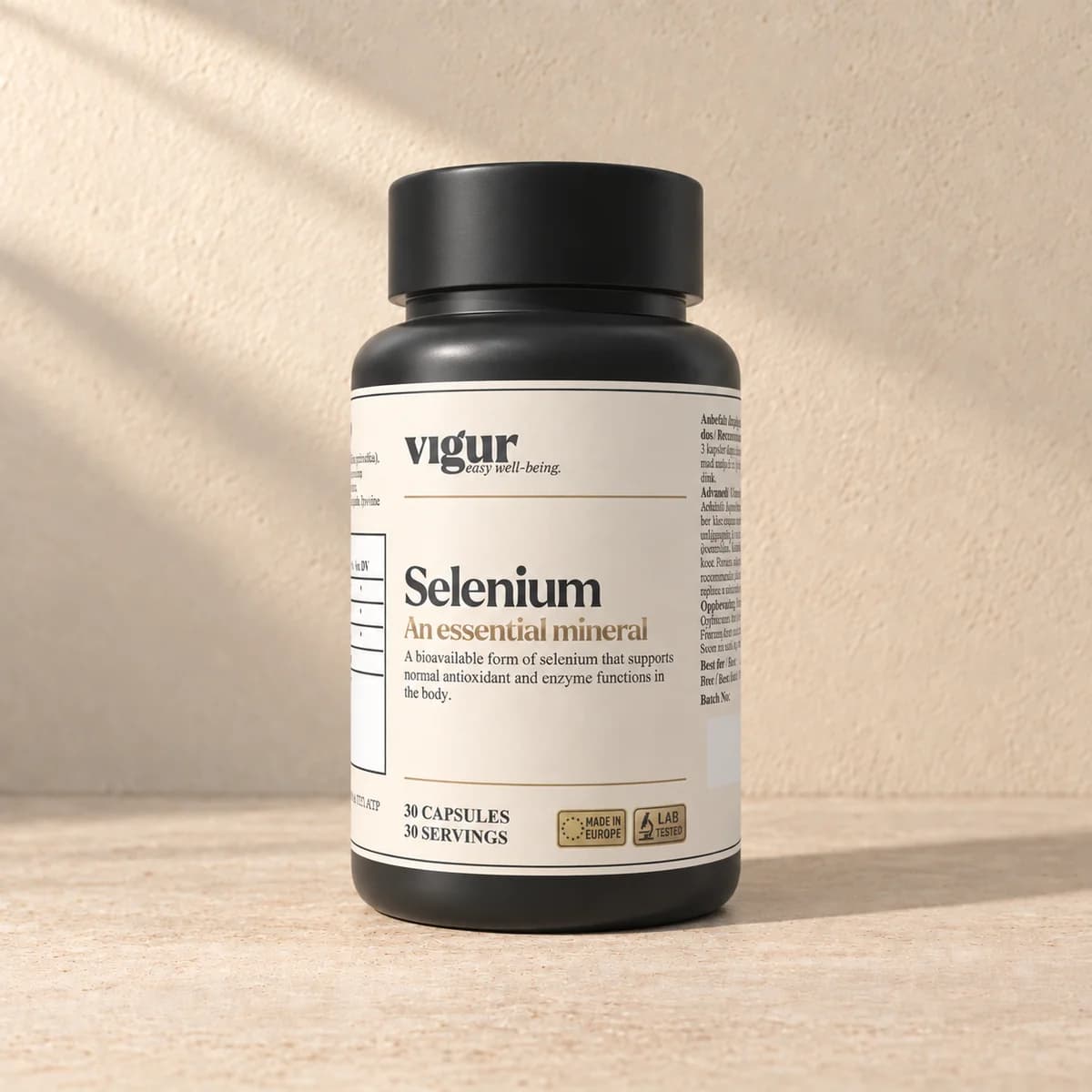 Svart tilskuddsboks med lys etikett merket Vigur og «Selenium» på beige bakgrunn