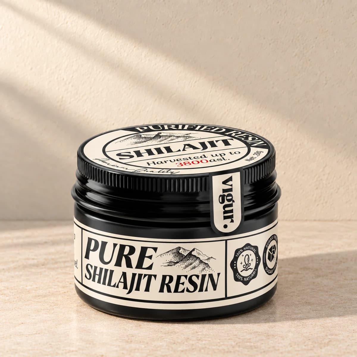 Svart rund boks med lokk og svart-hvit etikett «Pure Shilajit Resin» på beige bakgrunn