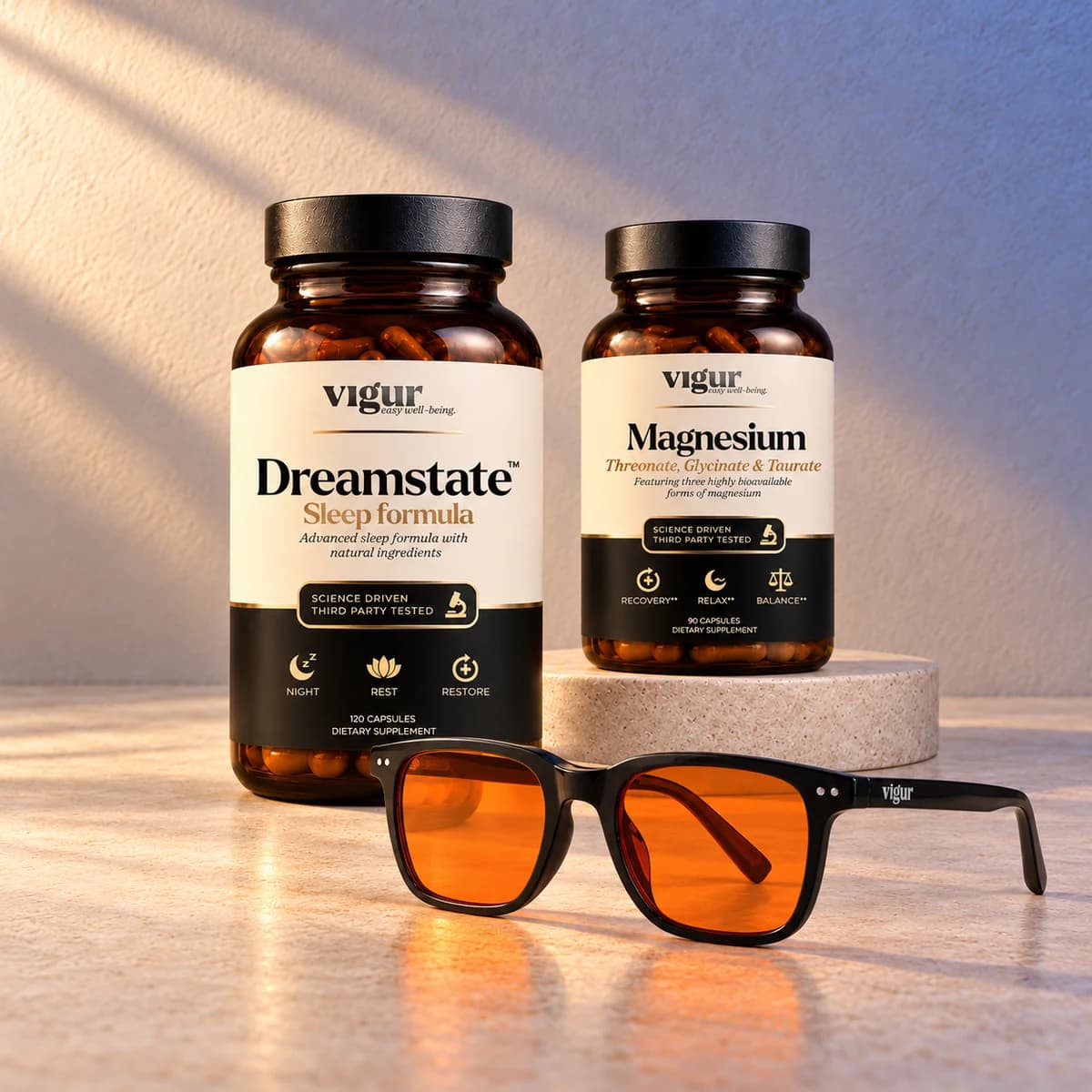 To mørke kapselbokser merket Vigur, «Dreamstate» og «Magnesium», på en lys sokkel med et par oransje blålysbriller foran, på varm bakgrunn