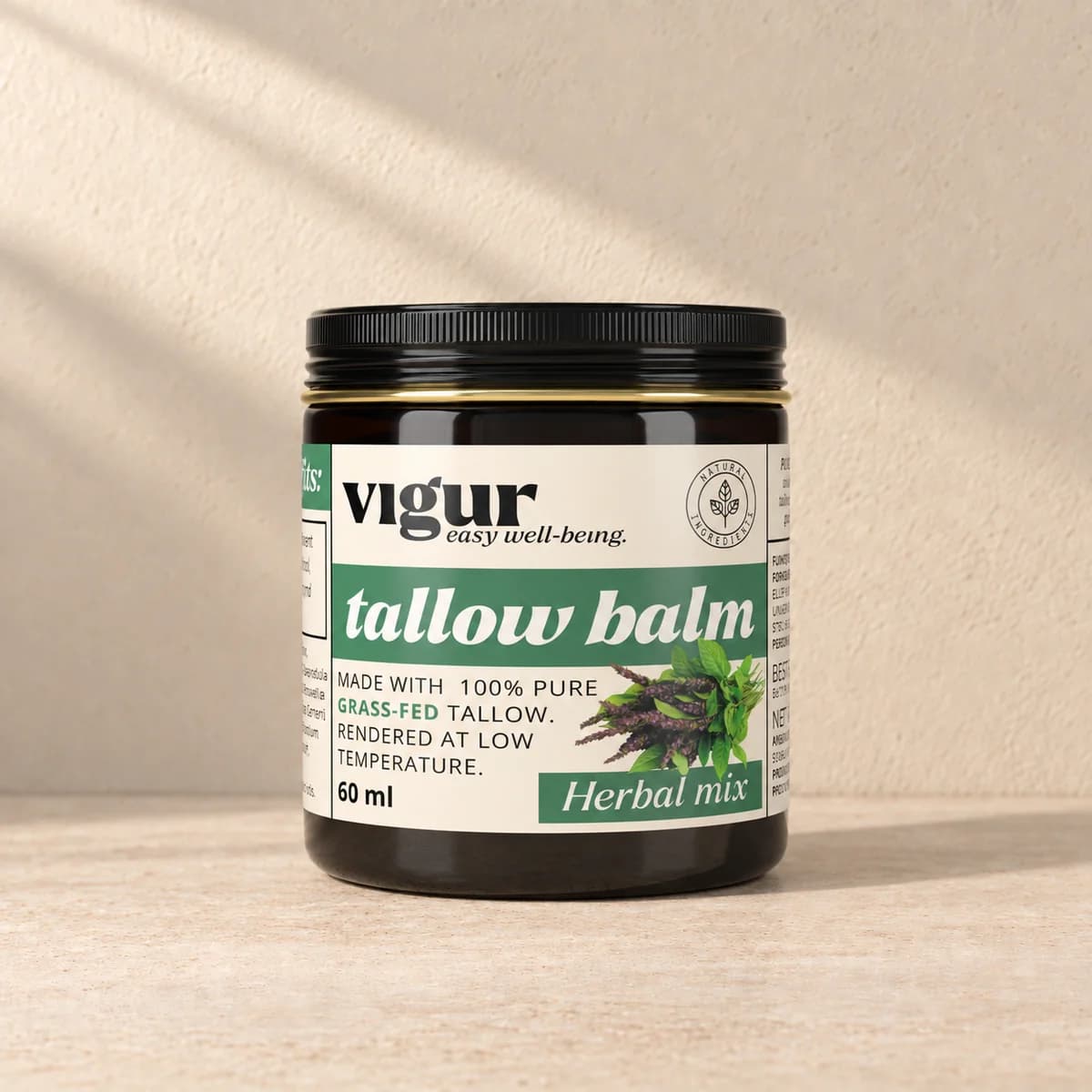 Svart boks med lys etikett merket Vigur og «Tallow balm Herbal mix» på beige bakgrunn