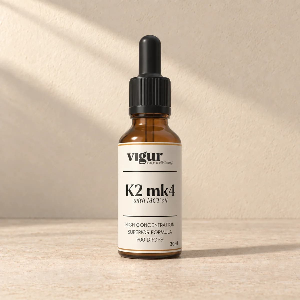 Liten brun glassflaske med pipettelokk og lys etikett merket Vigur og «K2 MK4» på beige bakgrunn